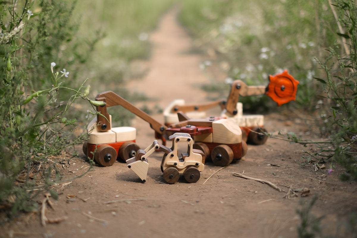 Maple Digger on a dirt path in front of three larger Oak & Sprout wooden vehicles, including the trench digger with its padauk cutter wheel