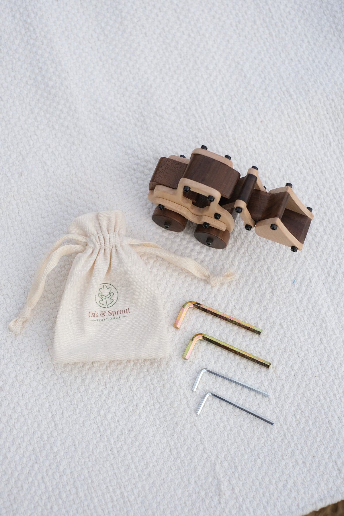 Maple Digger seen from above with four child-size Allen keys and an Oak & Sprout cotton drawstring pouch on a white textured throw