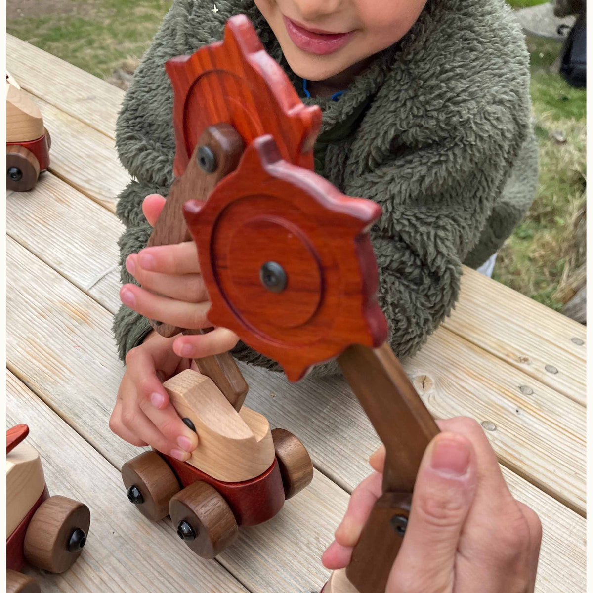 Child holding Padauk & Maple Trench Digger cutter wheel assembly outdoors, showing coral Padauk, dark Walnut, and cream Maple