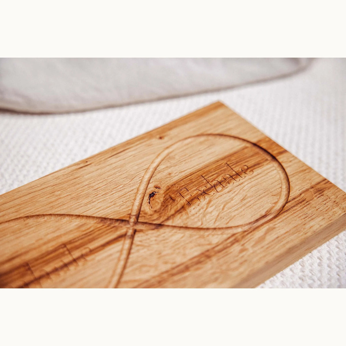 Action Oak donation — Infinity Board in honey-golden oak with routed infinity symbol and engraved text, on white waffle linen