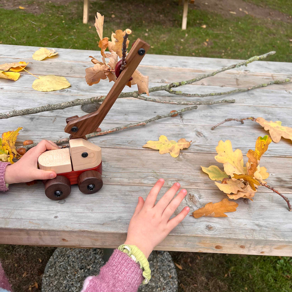 Child's hands playing with Walnut & Maple Crane outdoors, maple body, walnut boom and wheels, padauk base, autumn leaves near