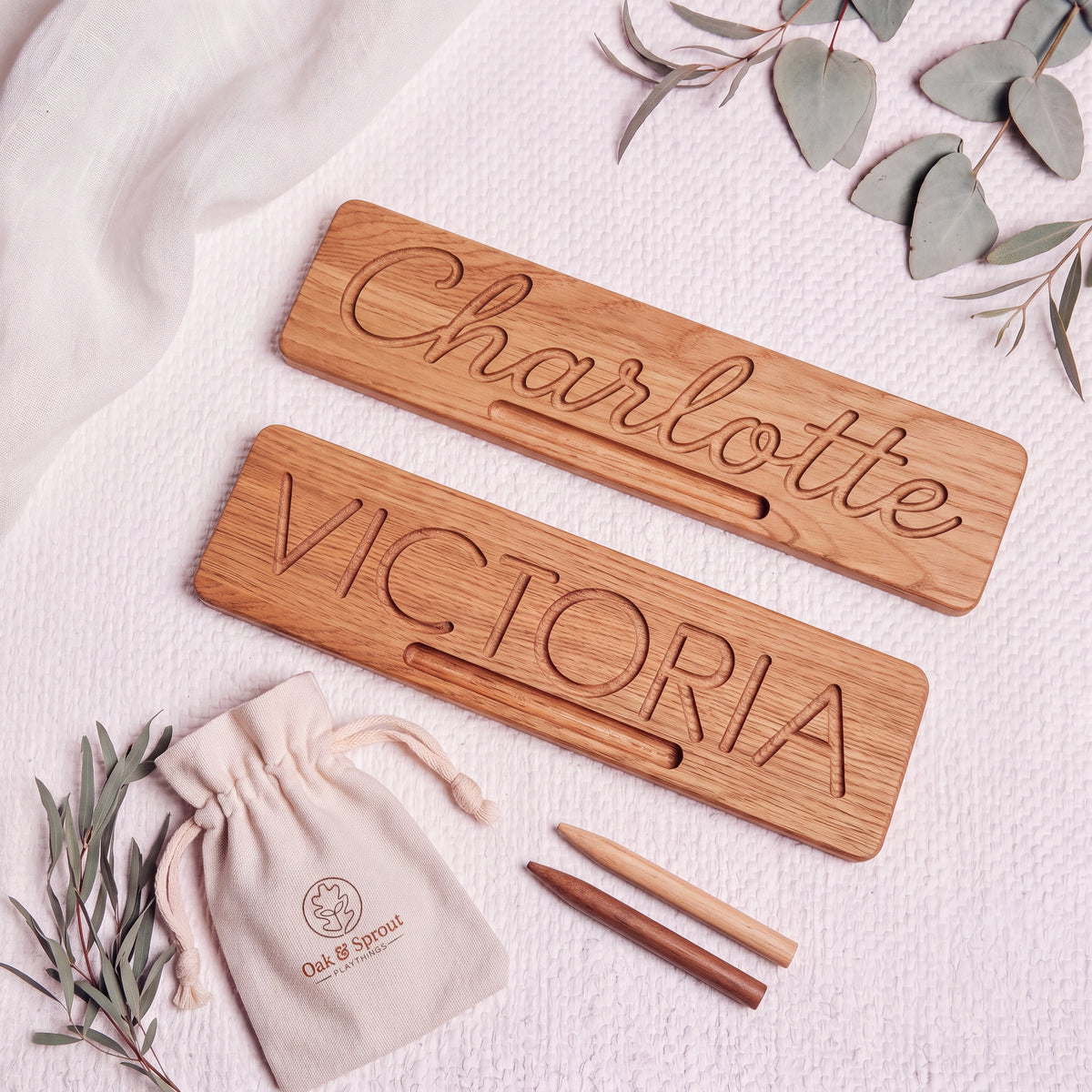 Two solid oak name tracing boards, Charlotte in cursive and VICTORIA in printed capitals, with an oak and a walnut stylus and an Oak & Sprout cotton pouch