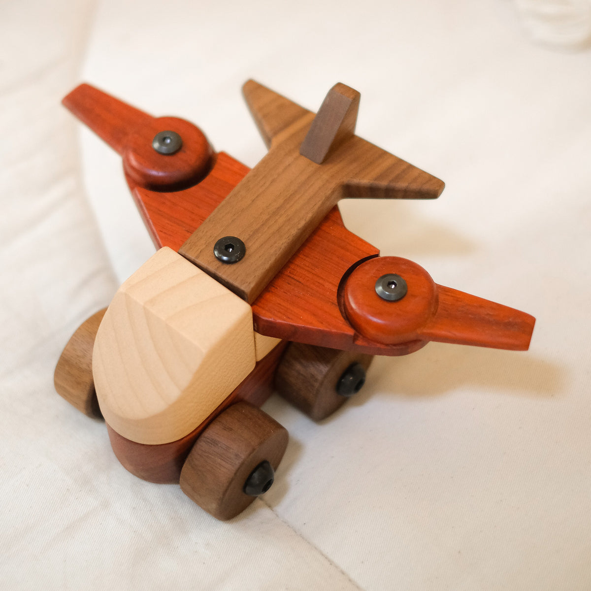 Walnut & Padauk Aeroplane close up on a cream cushion, padauk wings and propellers, walnut tail and wheels, pale maple nose