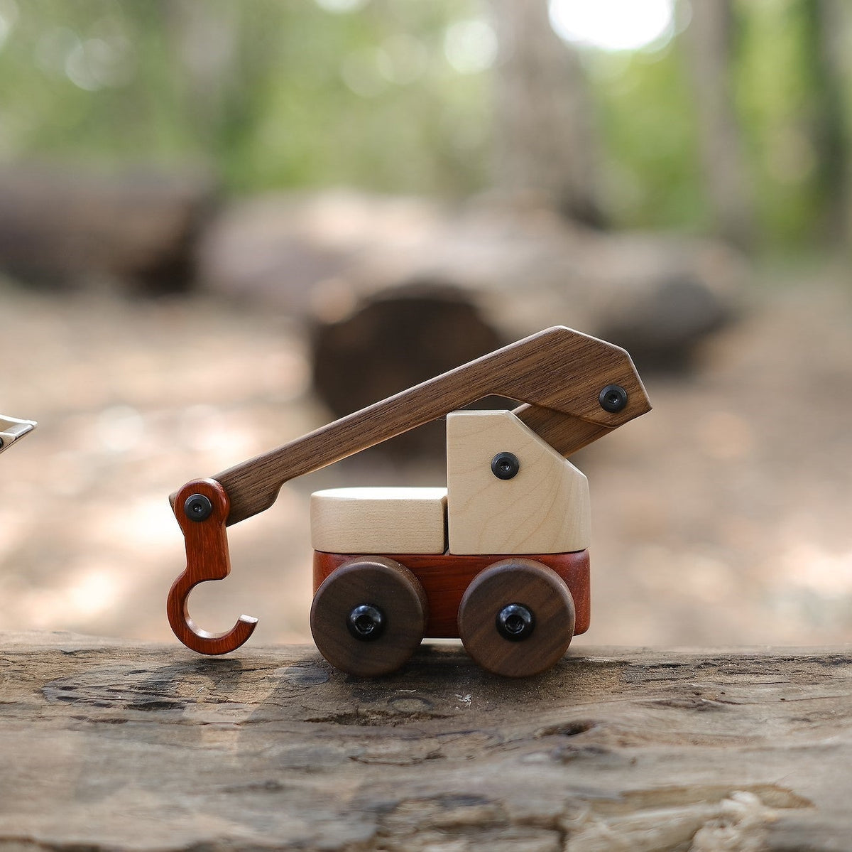 Crane Vehicle in maple and walnut with a padauk body and hook, jib raised, standing on a weathered log outdoors