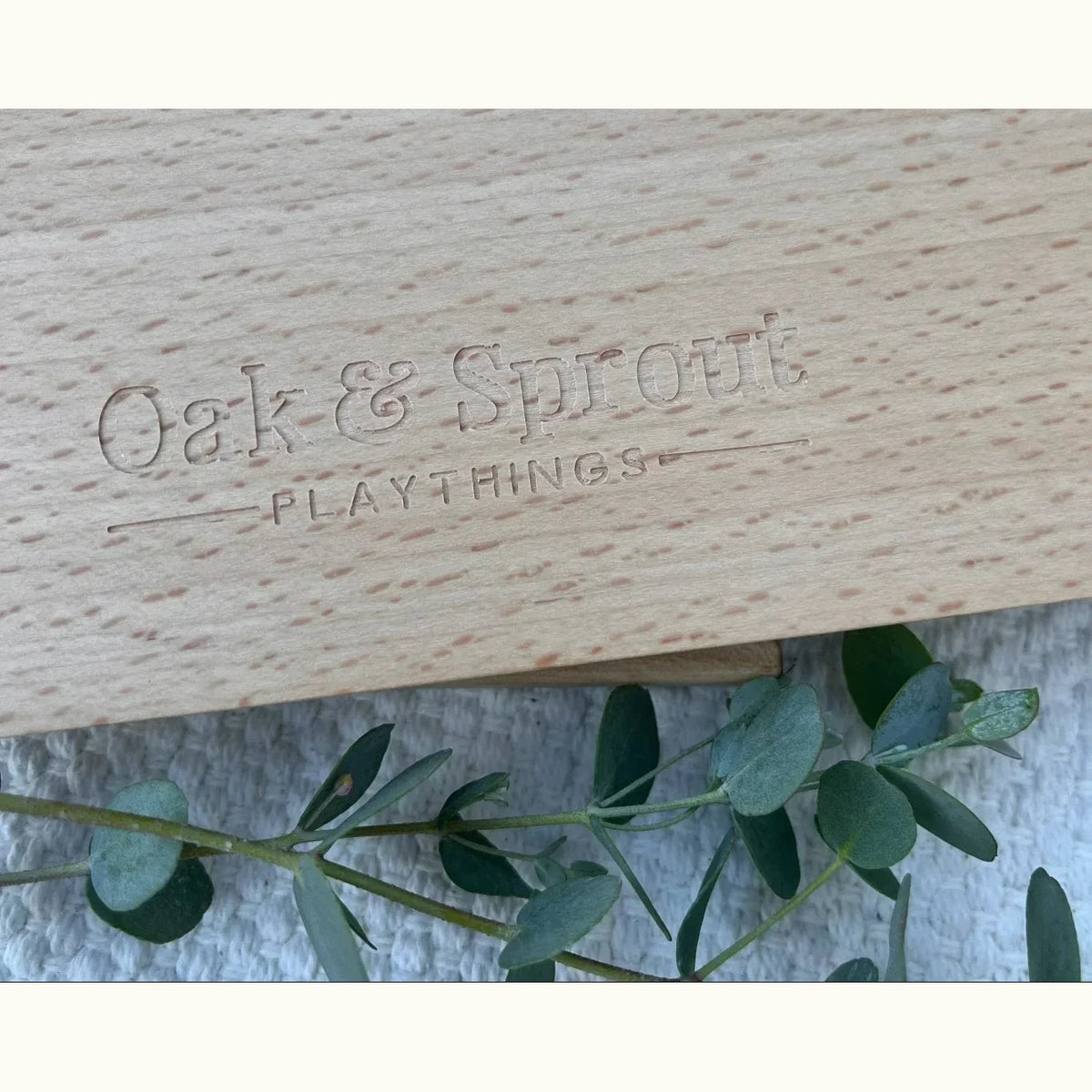 Oak & Sprout Playmat maple board back showing laser-engraved brand logo on pale cream fine-grained wood