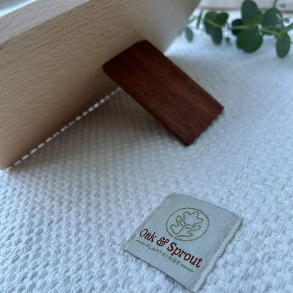 Close-up of Oak & Sprout label on white waffle playmat beside dark mahogany or walnut piece from Shelly Slow turtle puzzle