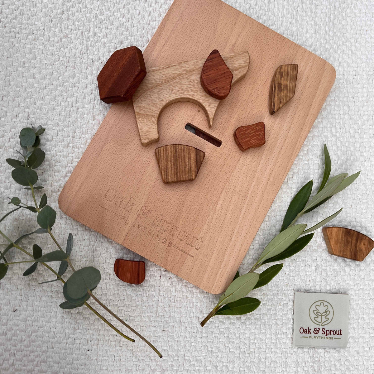 Sky Bloom balloon puzzle fully disassembled, padauk, walnut and zebrano pieces scattered around empty beech frame on linen ma