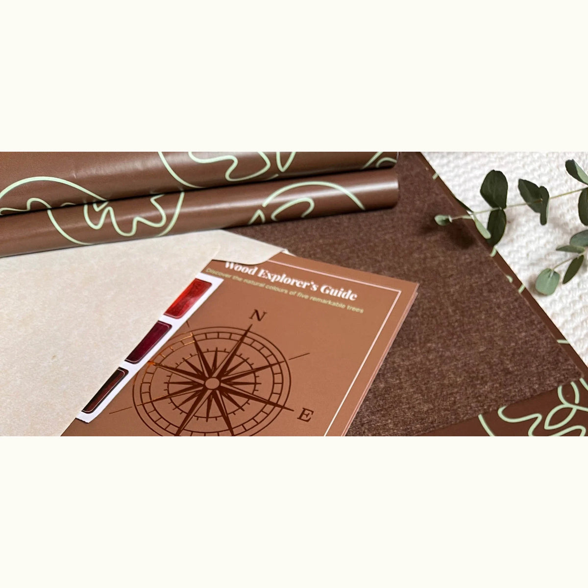 Infinity Breathing Board packaging: botanical-print wrap, kraft envelope, and Wood Explorer's Guide booklet with compass rose