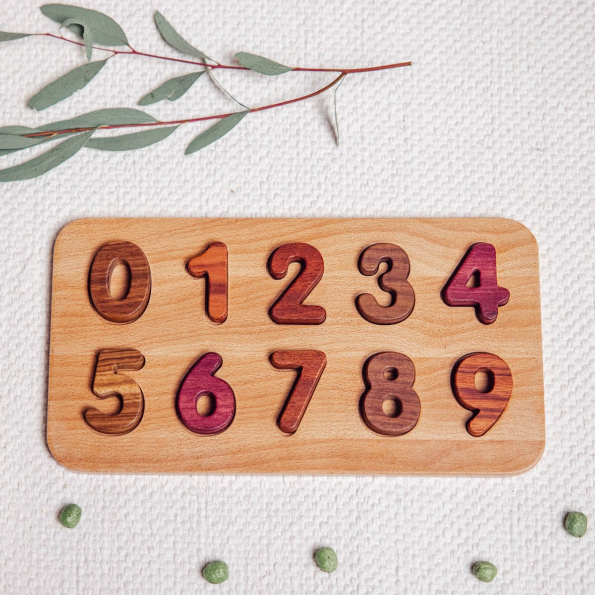 Wooden Number Puzzle 0–9 assembled flatlay showing Purpleheart, Walnut, Tigerwood and Mahogany pieces on linen