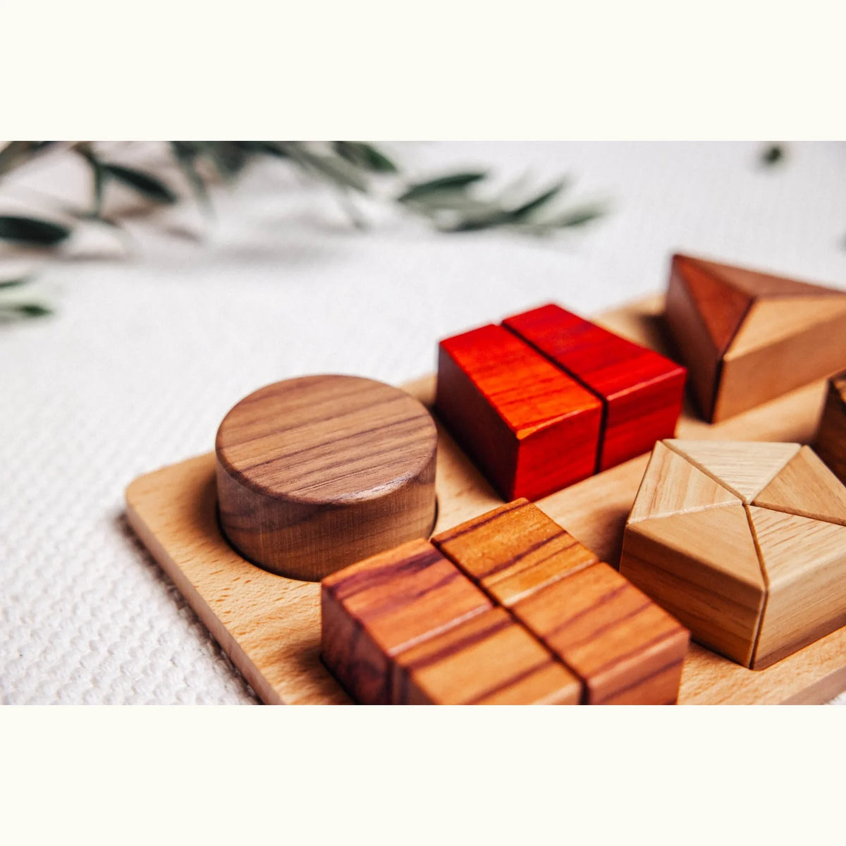 Geo Nest puzzle pieces on tray: walnut cylinder, padauk cubes, tigerwood striped cubes, rubberwood tray, linen surface