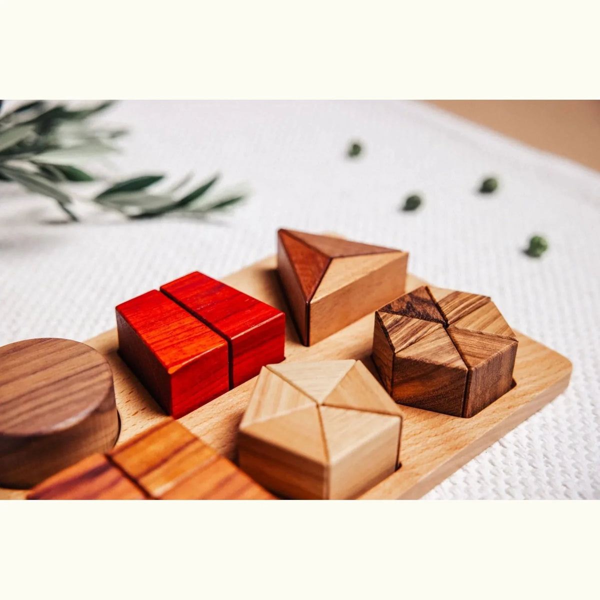 Geo Nest puzzle pieces semi-disassembled on linen mat: coral Padauk square, striped Zebrano hex, warm Tigerwood triangle