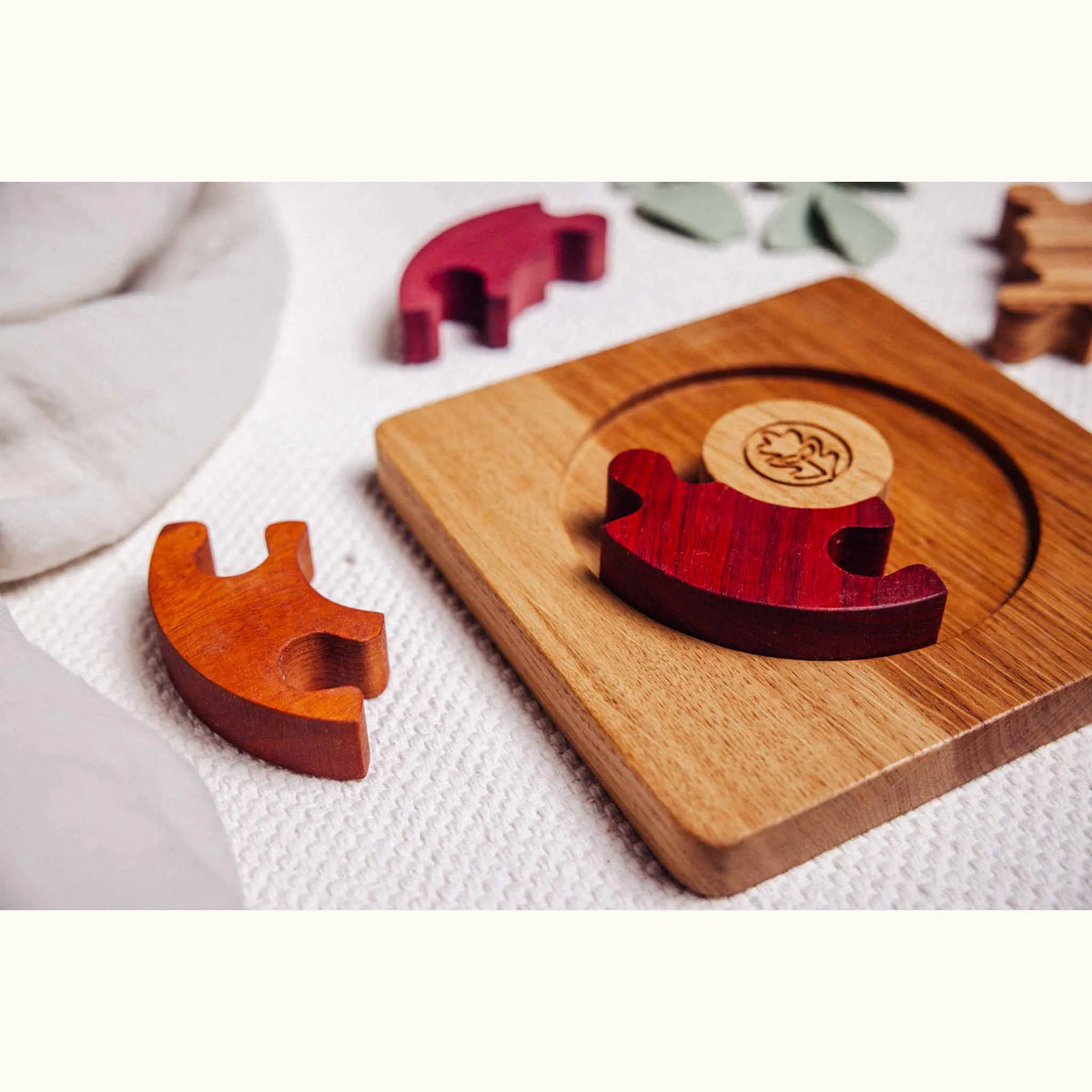 Unity Puzzle mid-play on linen mat: oak base with purpleheart disc and padauk segment placed, tigerwood piece removed alongsi