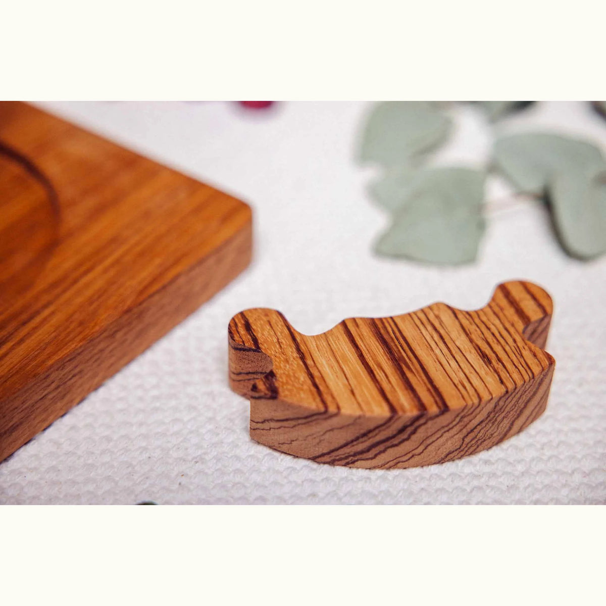 Unity Puzzle single Zebrano piece removed, showing bold orange-brown linear grain, with oak base board softly blurred beside 