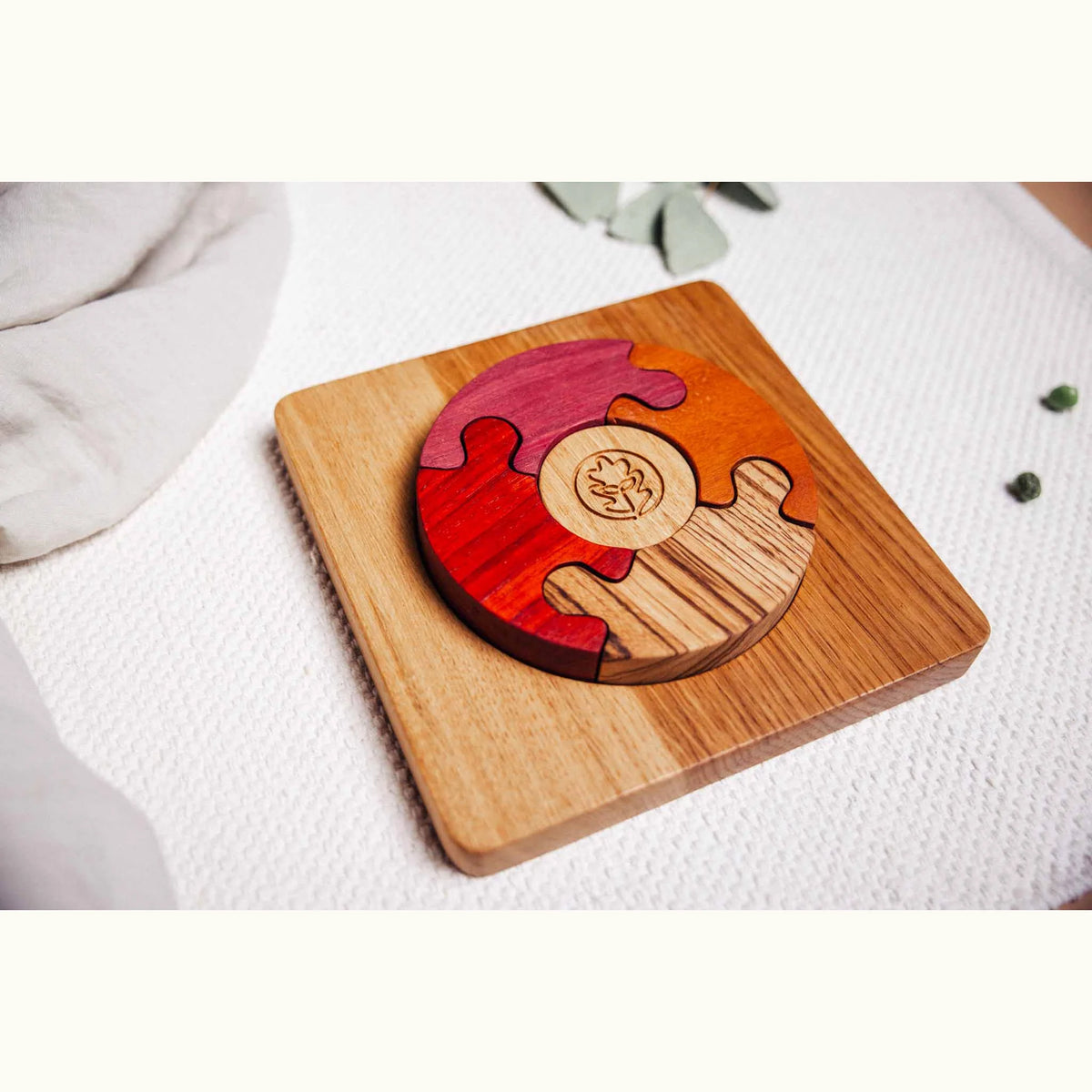 Unity Puzzle assembled on white playmat showing Purpleheart, Padauk, Tigerwood and Oak segments with engraved central disc